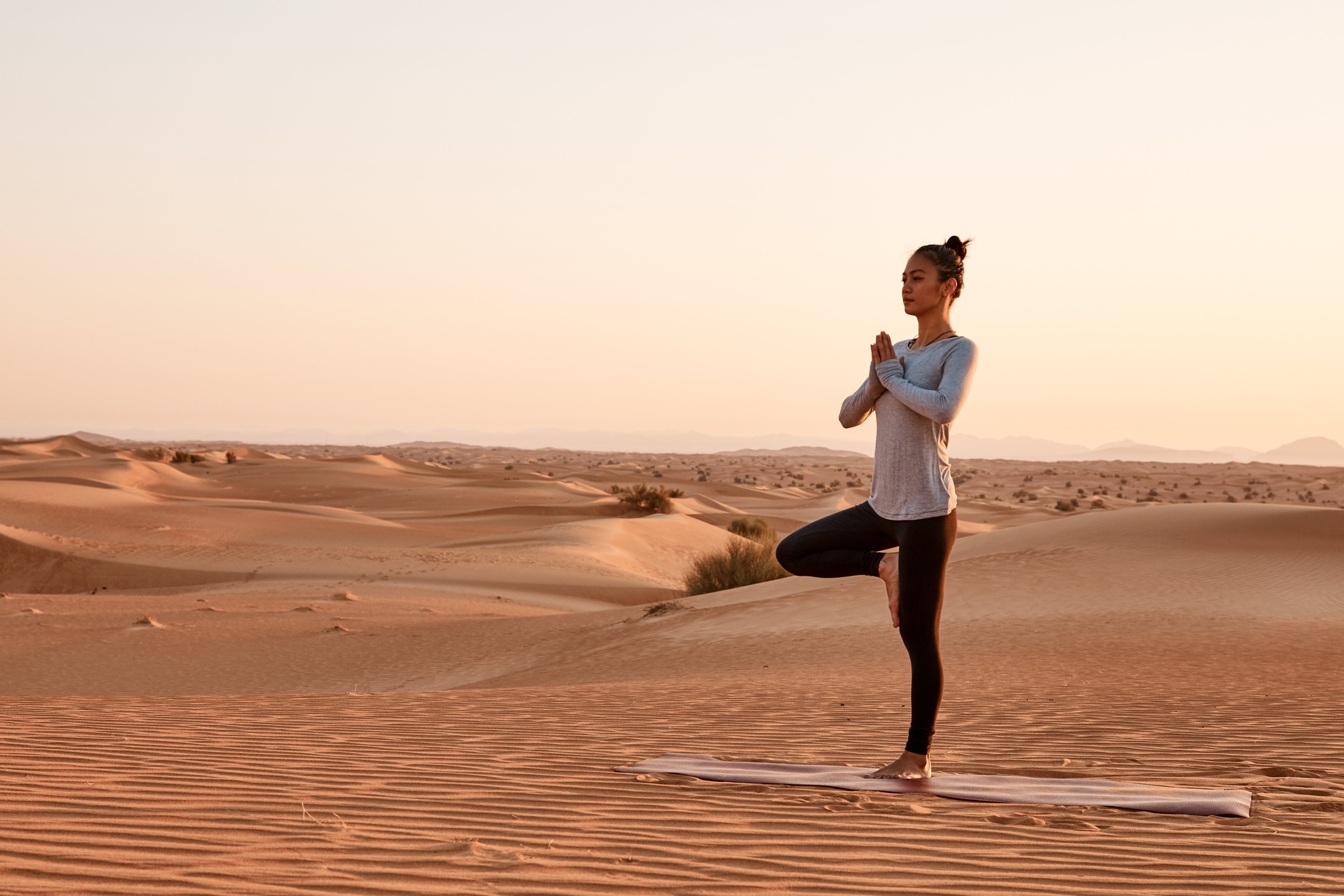 A woman practicing yoga on a mat in a glowing desert landscape at Al Maha