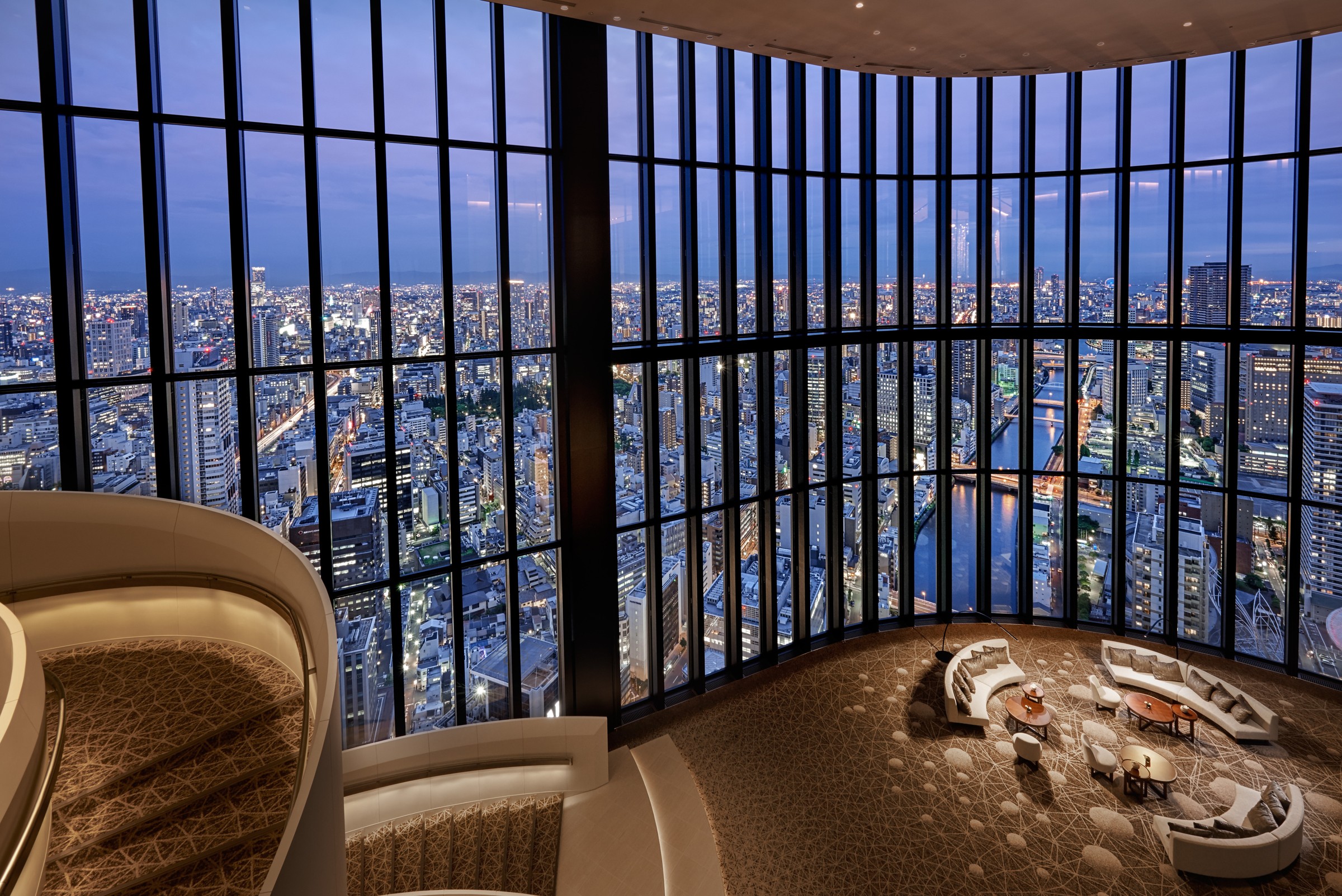 Conrad Osaka’s curved staircase and lounge facing a broad evening skyline