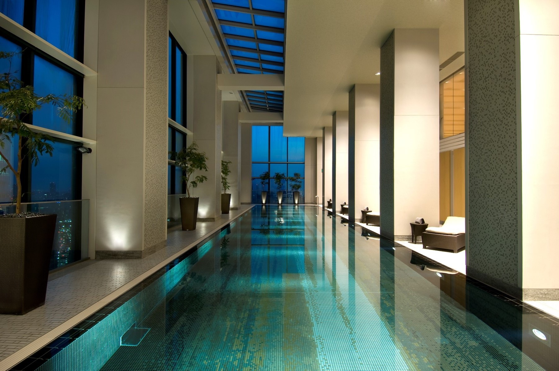 Illuminated indoor swimming pool beside tall windows at Conrad Tokyo