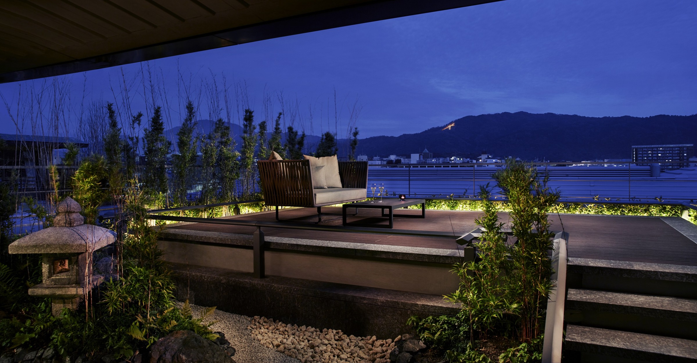 A garden terrace with seating, stone lanterns and mountain views at The Ritz-Carlton Kyoto at dusk
